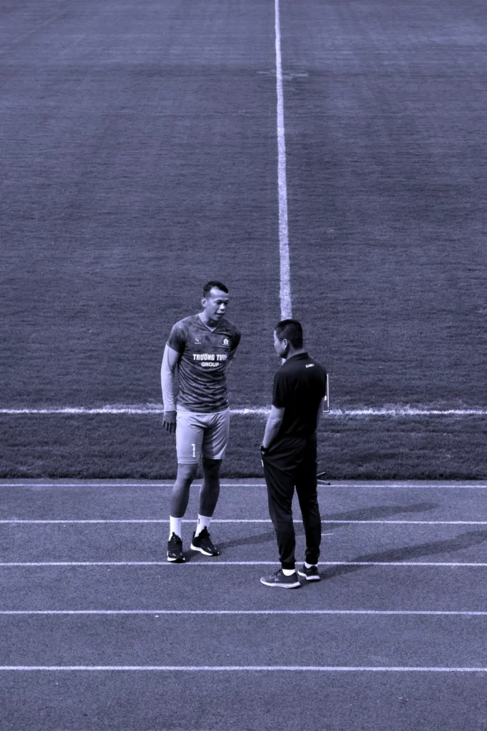 Deux sportifs échangeant sur une piste d'athlétisme, symbolisant l'approche stratégique et l'accompagnement personnalisé de l'investissement.