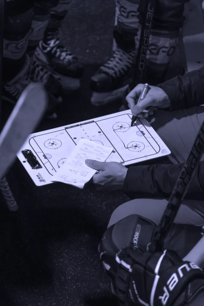 Vue rapprochée d'un entraîneur de hockey dessinant une tactique sur une ardoise, illustrant l'élaboration de plans de croissance et l'accompagnement stratégique des dirigeants.